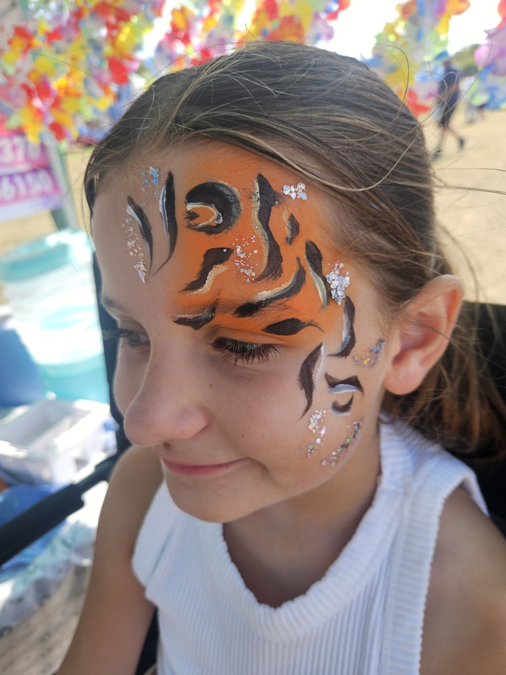 Orange tiger face painting with black stripes and glitter