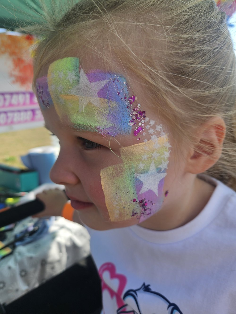 Pastel rainbow face painting with white stars and pink glitter