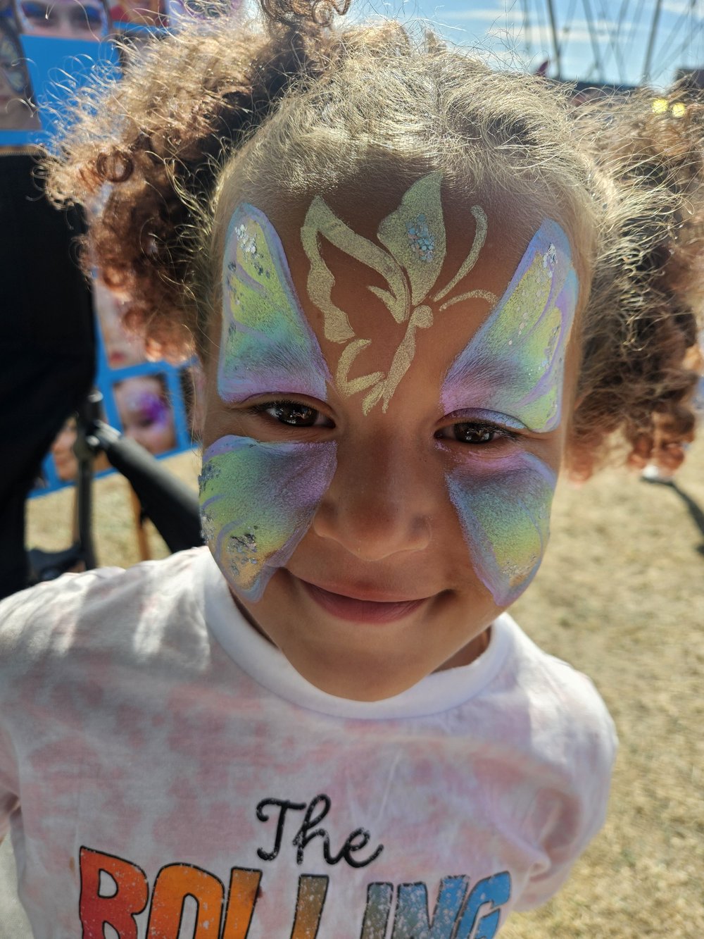 Pastel butterfly face painting with a fairy silhouette and blue gems